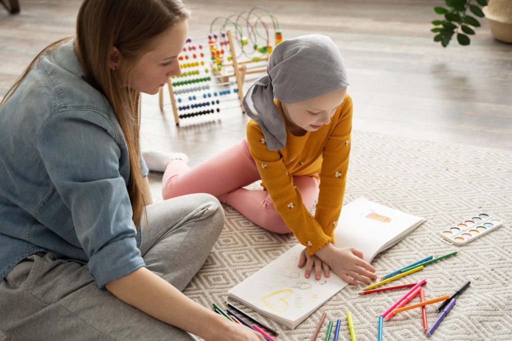 Menina paciente oncológica participando de atividades lúdicas de Psicanálise Infantil, colorindo desenhos com a psicanalista ao seu lado.