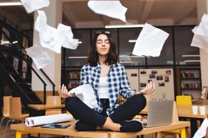 Jovem professora em pose de meditação, cercada de folhas de caderno.
